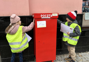 Dzieci wrzucają listy do skrzynki pocztowej.