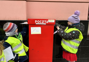 Dzieci wrzucają listy do skrzynki pocztowej.