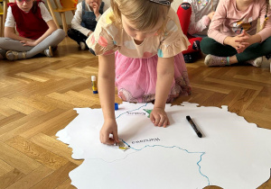 Dziewczynka przykleja obrazek na mapę Polski.