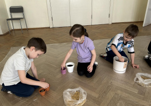 Dzieci wrzucają nasiona do doniczek.