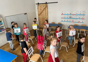 Dzieci stoją przy krzesłach z kropkami.