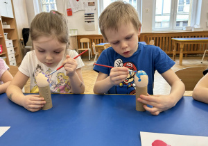Dzieci malują farbami jajka.