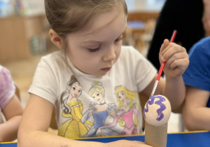Dziecko maluje farbami jajko.
