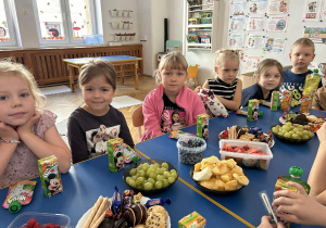 Dzieci z grupy czwartej siedzą przy stoliku i się uśmiechają.