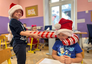 Chłopiec trzyma w ręku balon - laskę świąteczną. Chłopiec założył balon na szyję drugiego chłopca.