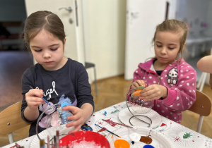 Dziewczynki z grupy czwartej malują farbami bombki szklane.