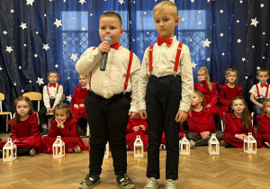 Na środku sali stoją chłopcy. Jeden z nich trzyma mikrofon, mówi wiersz - powitanie gości.