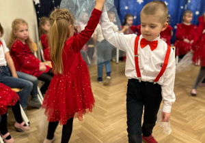 Dzieci z grupy trzeciej tworzą parę. Trzymają w rękach biało - niebieskie chusty. Kręcą się w kółko.