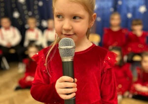 Dziewczynka stoi na środku sali, trzyma mikrofon. Mówi wiersz.