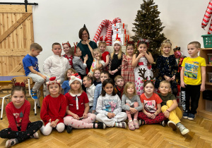 Zdjęcie grupowe - grupa czwarta. Część dzieci stoi, druga część dzieci siedzi. Na środku całej grupy stoi mama chłopca. Wszyscy na zdjęciu uśmiechają się.