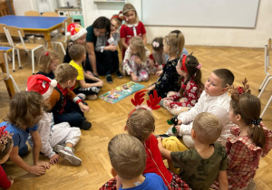 Dzieci siedzą w kole. Na środku koła siedzi mama chłopca. Kuba siedzi na kolanach mamy, która czyta książkę.