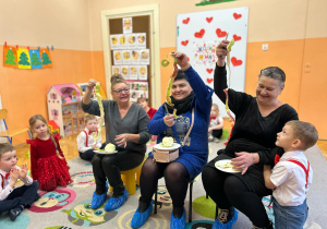 Babcie siedzą na krzesłach i pokazują obraną skórkę jabłka.