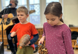 Chłopiec i dziewczynka stoją na sali i trzymają instrumenty, na których grają.