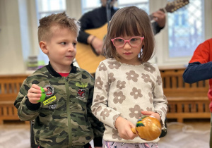 Chłopiec i dziewczynka stoją na sali i trzymają instrumenty, na których grają.