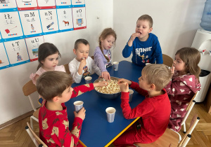 Dzieci siedzą przy stoliku i jedzą popcorn.