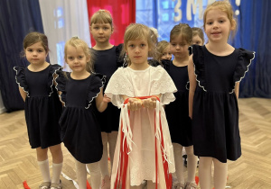 Zdjęcie grupowe- dziewczynki stoją w małej grupie, jedna z dziewczynek trzyma białe i czerwone wstążki.