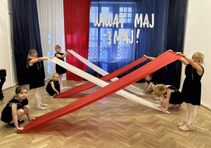 Dziewczynki trzymają dwie białe i czerwone chusty.