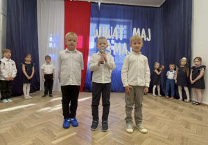 Trzech chłopców stoi na środku sali i jeden z nich mówi wiersz.