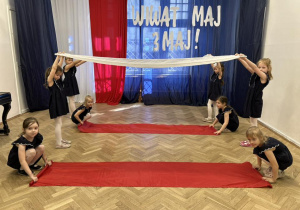 Dziewczynki trzymają dwie białe i czerwone chusty.
