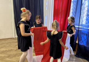 Dziewczynki trzymają dwie białe i czerwone chusty, tworzą małe kółeczko.