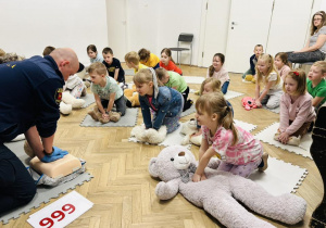 Dzieci z grupy IV uciskają klatkę piersiową misia.
