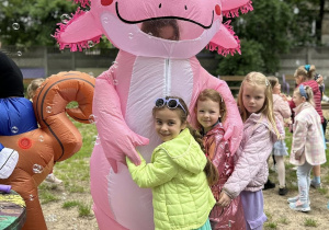 Dziewczynki przytulają się do różowego dinozaura.