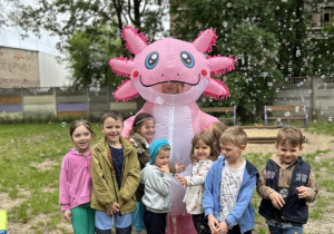 Dzieci uśmiechają się i przytulają do różowego dinozaura.