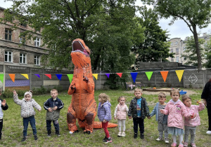 Dzieci tańczą w kole z dinozaurem.