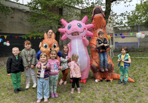 Dzieci pozują do zdjęcia z dwoma dinozaurami i wiewiórką.