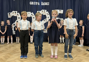 Czwórka dzieci stoi na scenie. Dziewczynka trzyma mikrofon i mówi wiersz.
