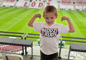 Chłopiec w koszulce ŁKS na tle trybun.
