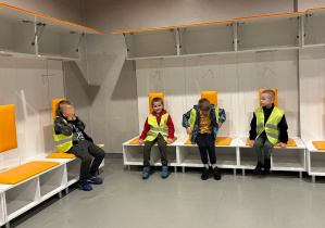 Dzieci siedzą w szatni piłkarzy.
