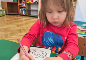 Dziewczynka koloruje kolorowankę z psem.