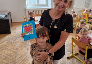 Wspólne zdjęcie pracownika przedszkola z dzieckiem. Dziecko wręczyło laurkę Pani.