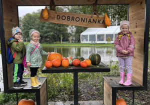 Dzieci stoją na dużych krzesłach przy stoliku z dyniami.
