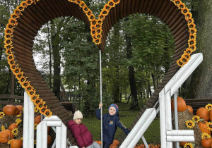 Dziewczynka i chłopiec stoją w wielkim sercu z dyniami.