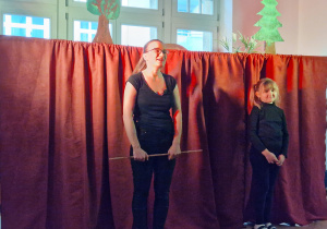 Pani z teatrzyku i dziewczynka stoją na tle czerwonej kurtyny.