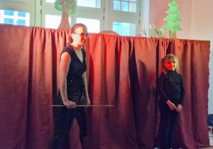 Pani z teatrzyku i dziewczynka stoją na tle czerwonej kurtyny.