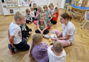 Dzieci podzielone na małe grupy, siedzą w małych grupach. Jedna z grup zapoznaje się z misiem.