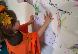 Dziewczynka przykłada dłoń do plakatu.