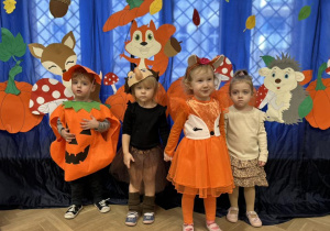 Dzieci z grupy I stoją w strojach jesiennych na tle dekoracji.
