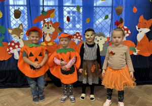 Dzieci z grupy II stoją w strojach jesiennych na tle dekoracji.