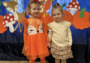 Dwie dziewczynki stoją ubrane w strojach jesiennych, na tle dekoracji.