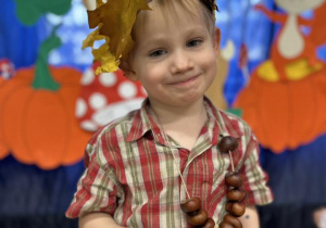 Chłopiec ubrany w stój jesienny, stoi na tle dekoracji.