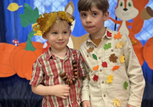 Chłopcy z grupy II ubrani w jesienne stroje stoją na tle dekoracji.