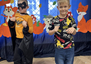 Dwóch chłopców stoi na tle dekoracji i tańczą.