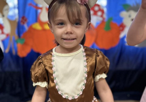 Dziewczynka z grupy IV ubrana w stój jesienny uśmiecha się do zdjęcia.