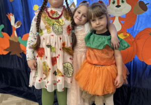 Dwie dziewczynki przytulają się do siebie. Stoją na tle dekoracji.