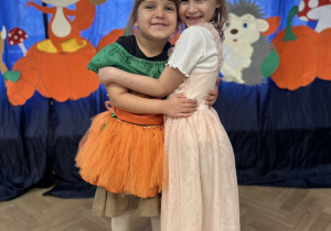 Dwie dziewczynki przytulają się do siebie. Stoją na tle dekoracji.