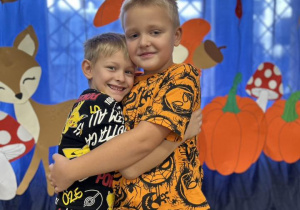 Dwóch chłopców przytula się do siebie. Stoją na tle dekoracji.